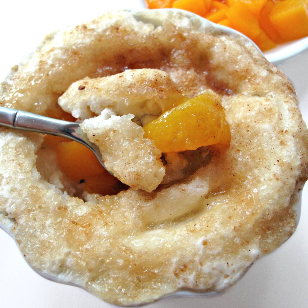 Spoon with peaches coming out of crust covered bowl.
