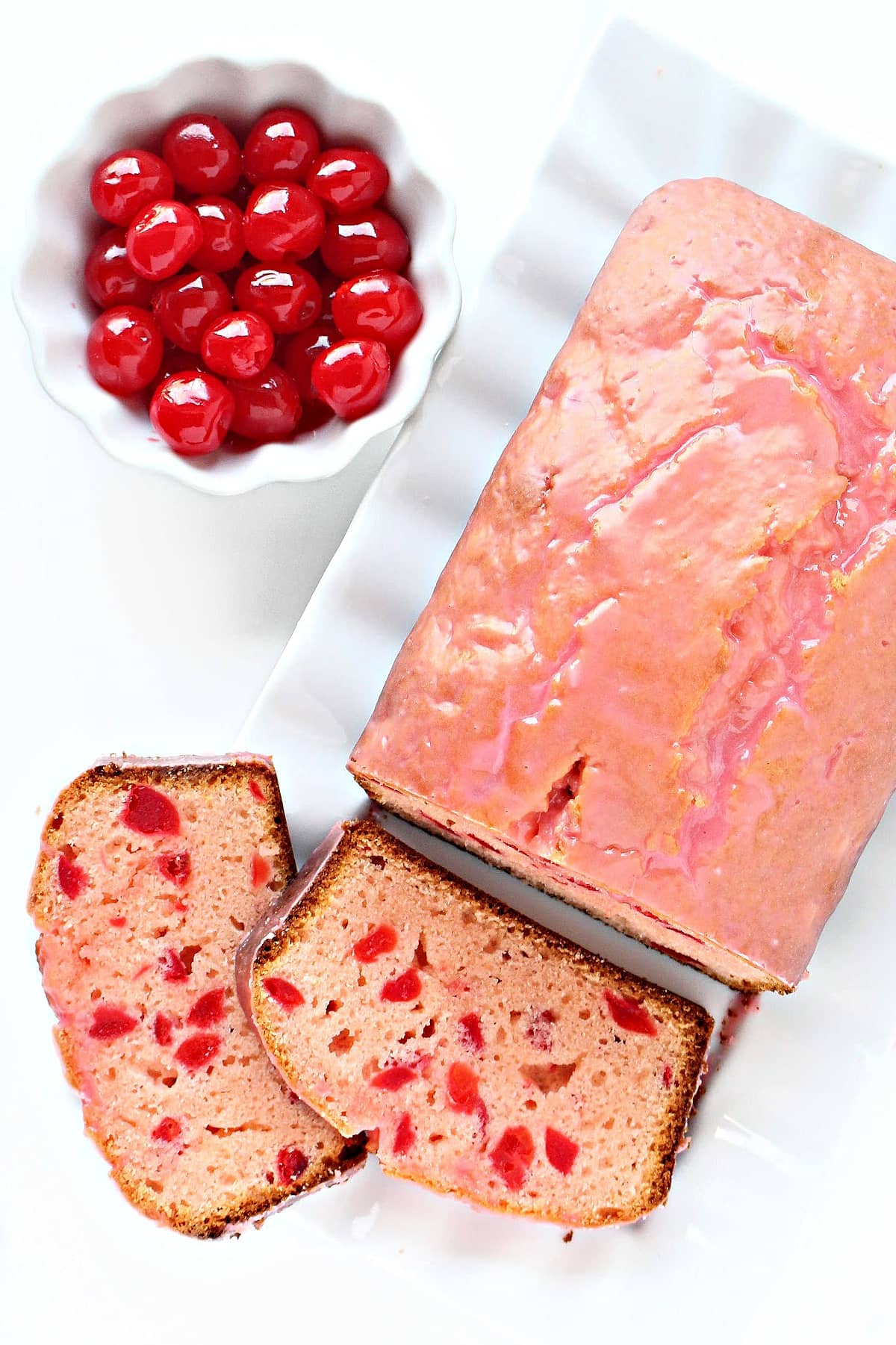 A pink glazed loaf cake and a bowl of maraschino cherries.