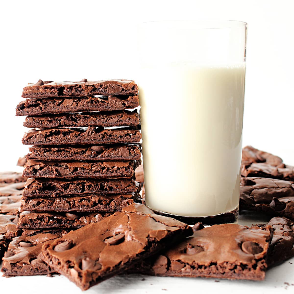 Stack of thin brownie brittle next to a glass of milk.