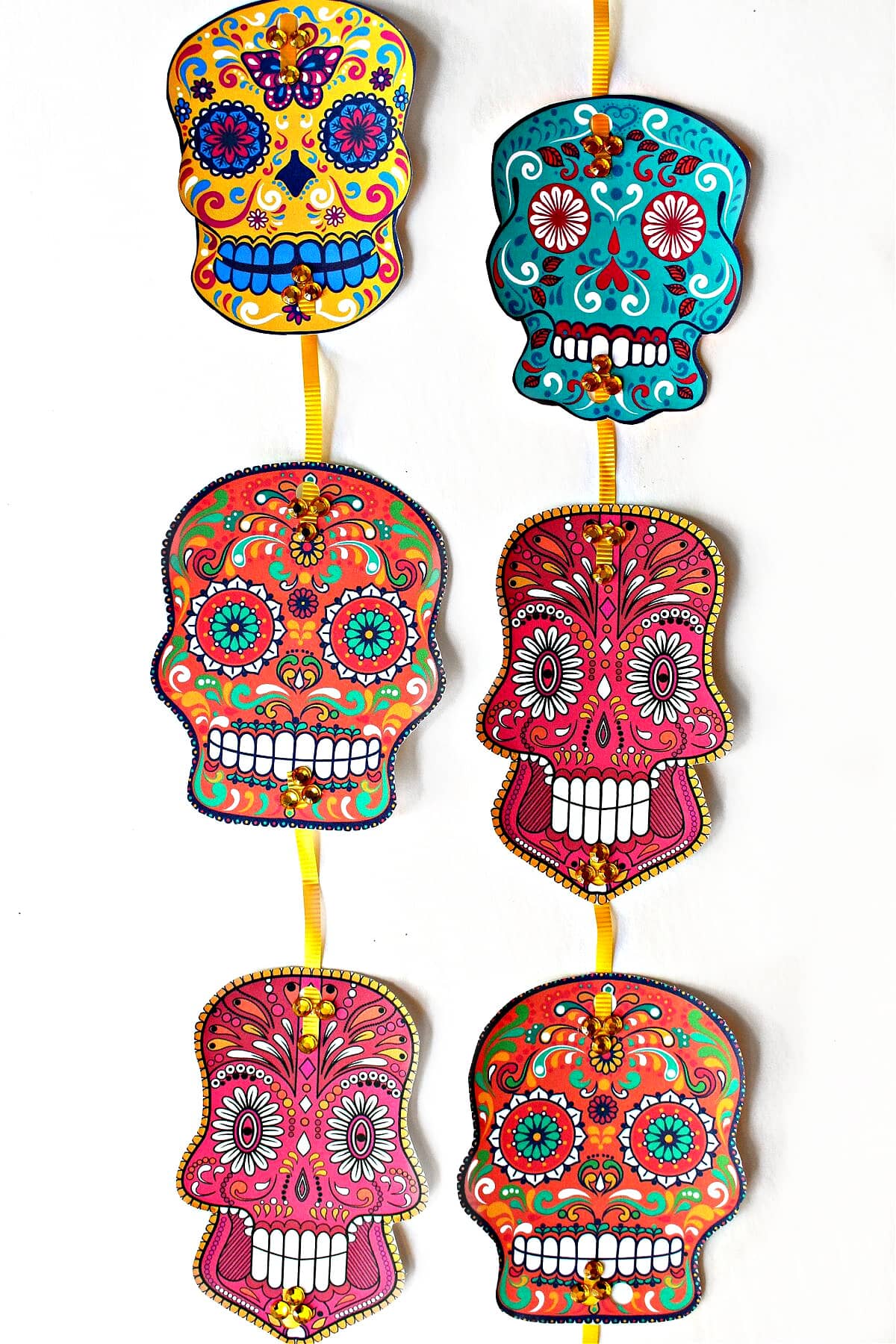 Two strings of colorful calavera skulls printed on cardstock.