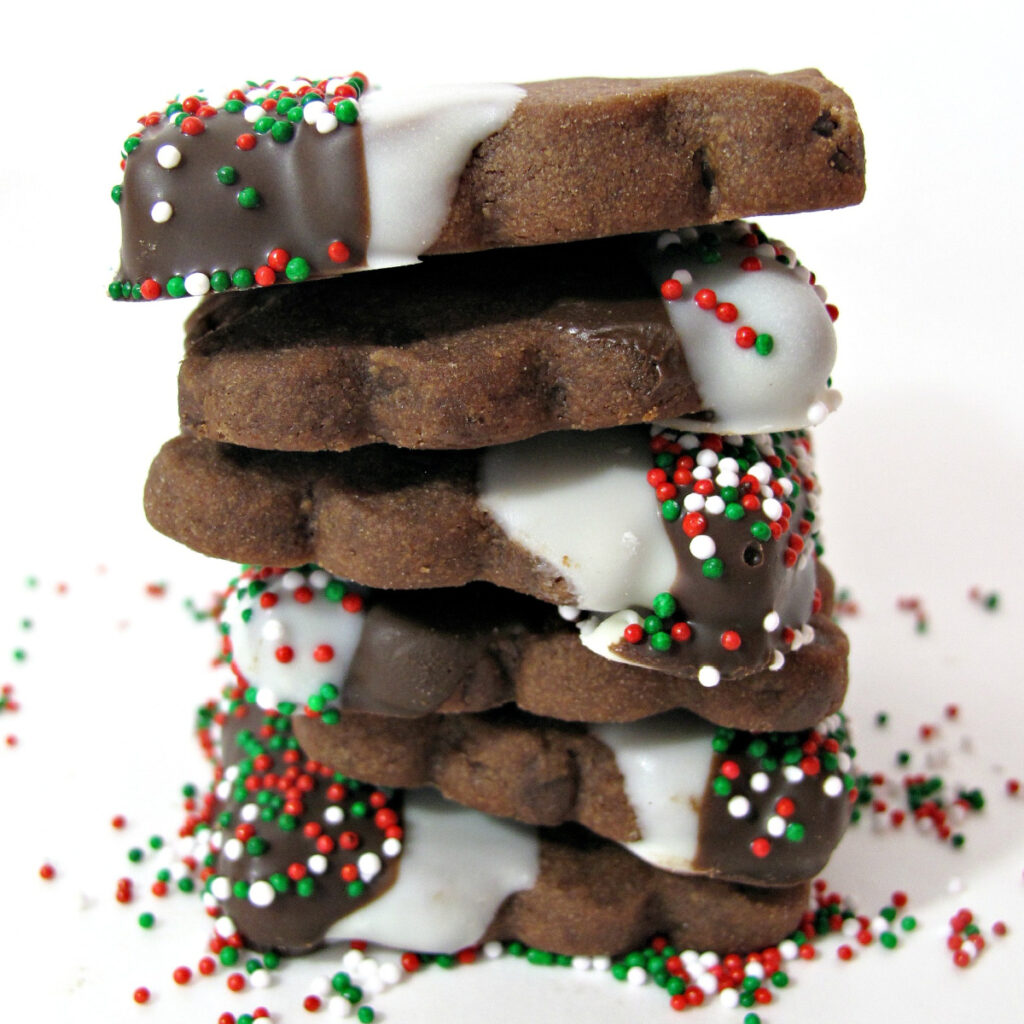 Stack of chocolate shortbread cookies with one end dipped in chocolate and sprinkles.