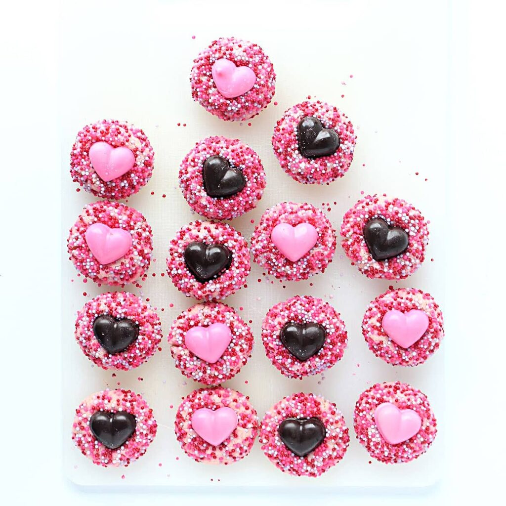 Thumbprint cookies coated in sprinkles with chocolate hearts in the centers.