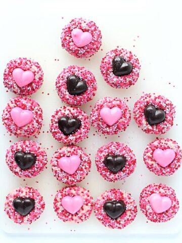 Thumbprint cookies coated in sprinkles with chocolate hearts in the centers.