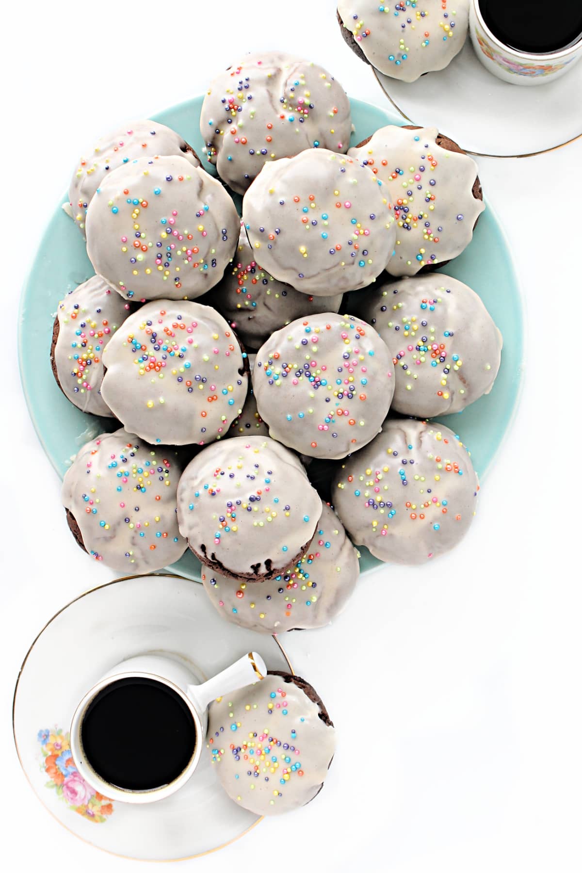 Puffy chocolate cookies with white icing and multicolored sprinkles on a plate.