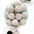 Iced chocolate cookies with sprinkles piled on a plate.