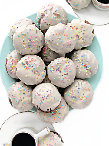 Iced chocolate cookies with sprinkles piled on a plate.