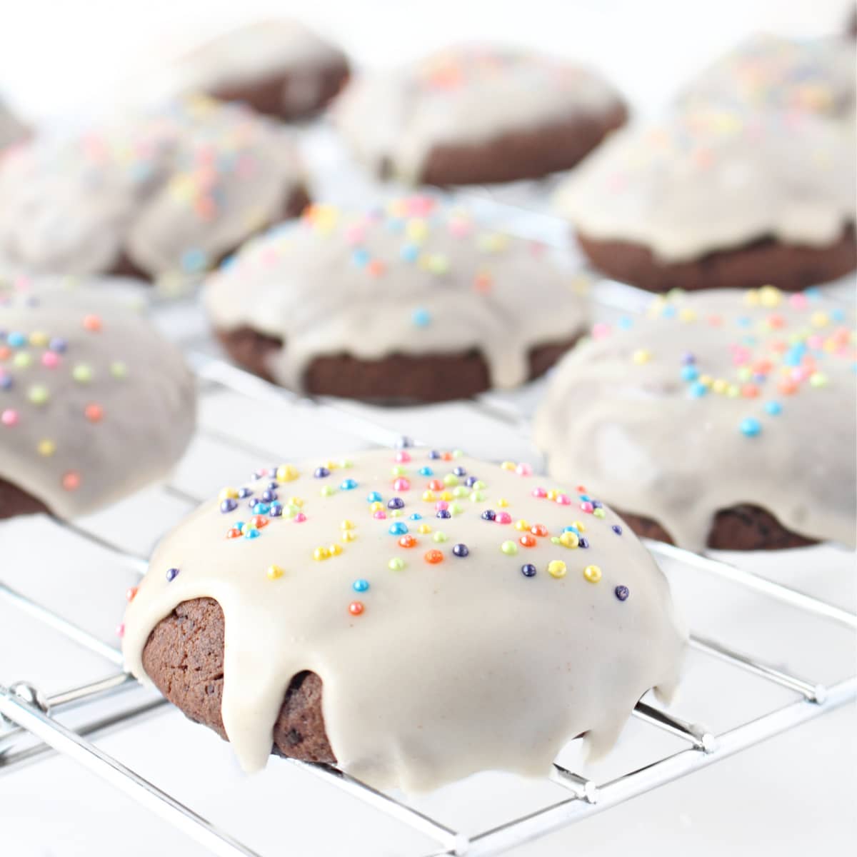 Closeup of chocolate cookie coated in white icing with multicolored nonpareil sprinkles.
