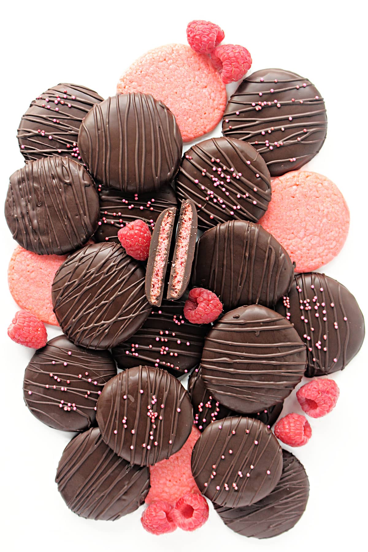 Thin, pink raspberry cookies coated in chocolate decorated with chocolate zigzags and sprinkles.
