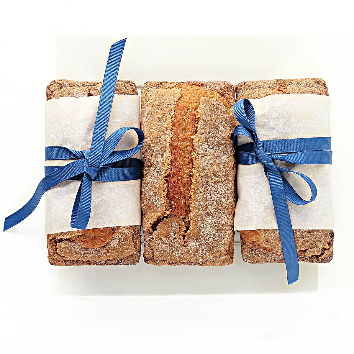 Three mini loaves on a plate, two wrapped with parchment and blue ribbon.