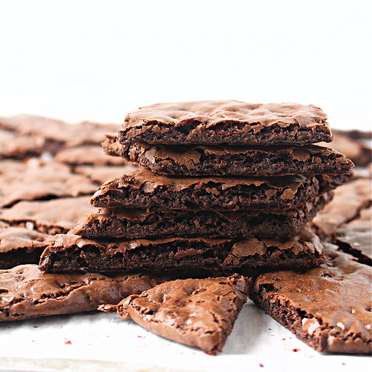 Stack of thin, crisp brownie cookies with shiny top crust.