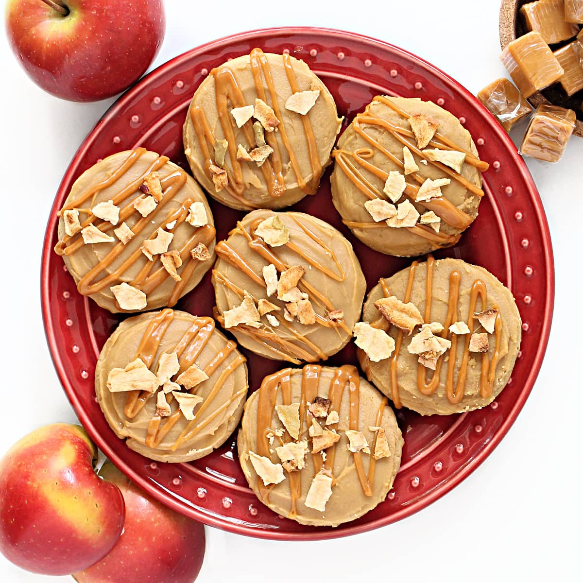 Frosted cookies, drizzled with caramel and dried apple chips on a red serving plate.