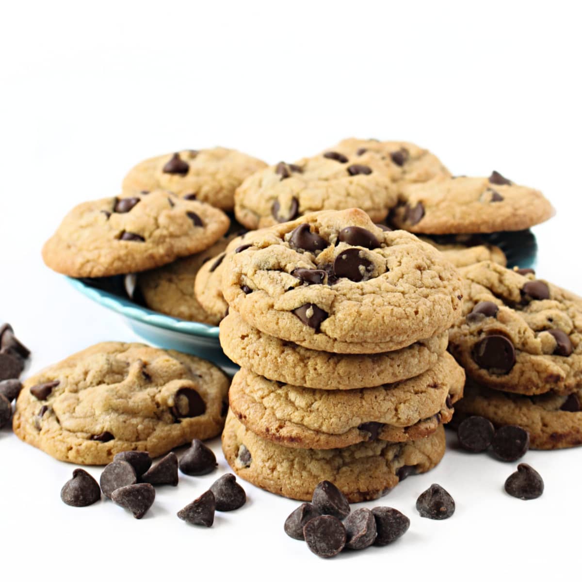 Stack of thick chocolate chip cookies in front of a plate of cookies.