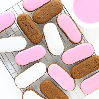 Pink and white iced oval Honey Jumble biscuits on a wire rack.