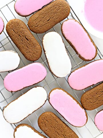 Pink and white iced oval Honey Jumble biscuits on a wire rack.