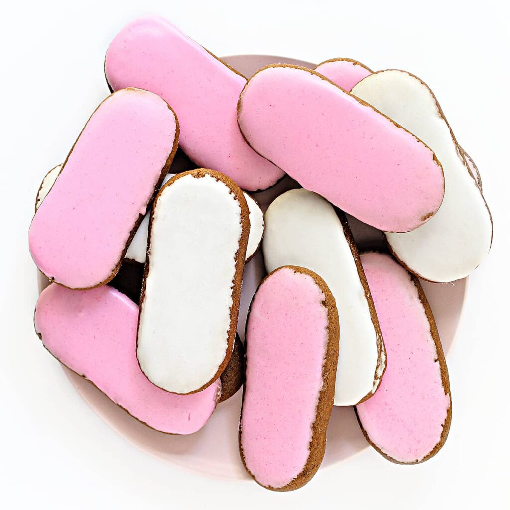 Long, thin oval cookies iced with thin pink and white icing on a serving plate.