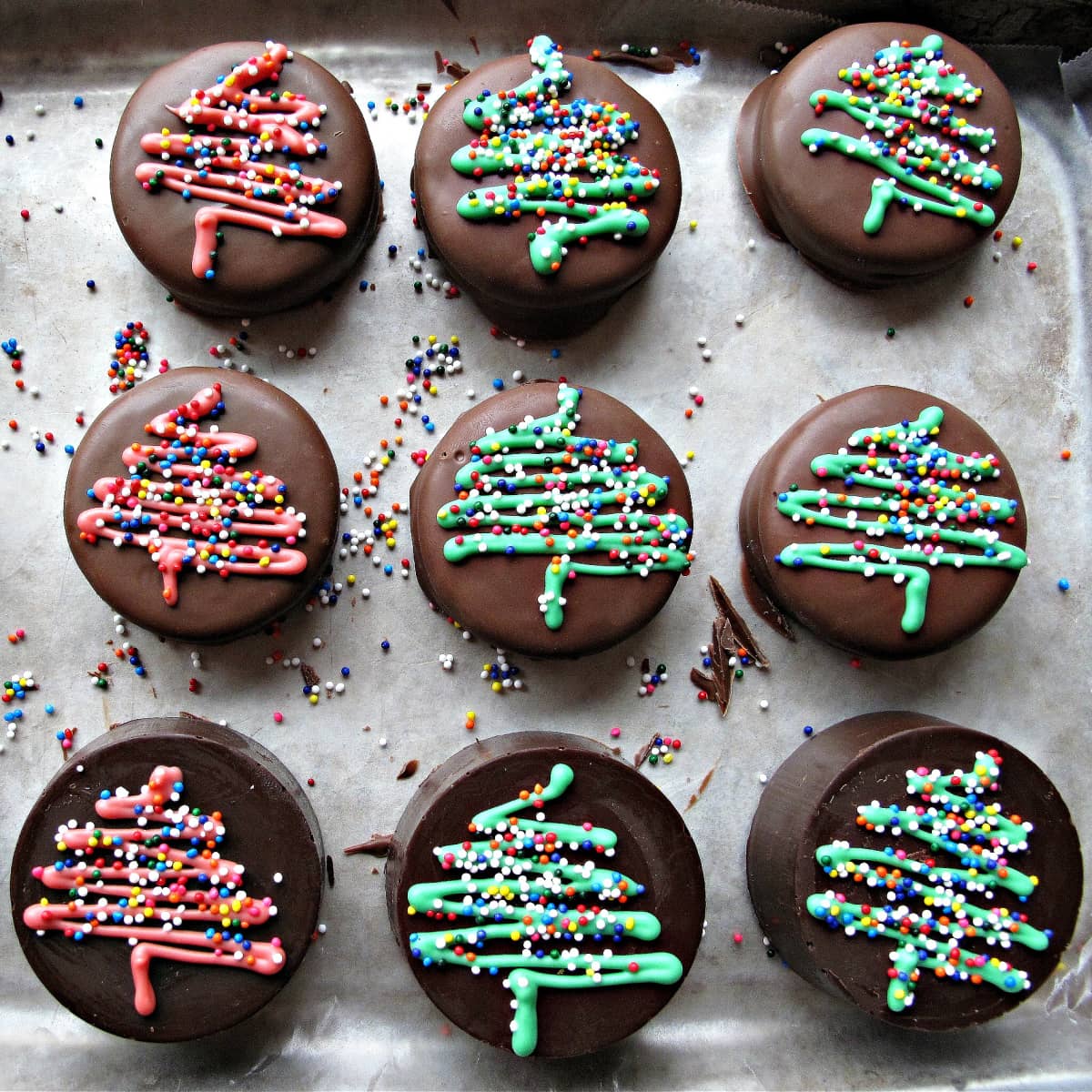 Chocolate covered Oreos decorated with red and green zigzag Christmas trees with multicolored nonpareil sprinkles.