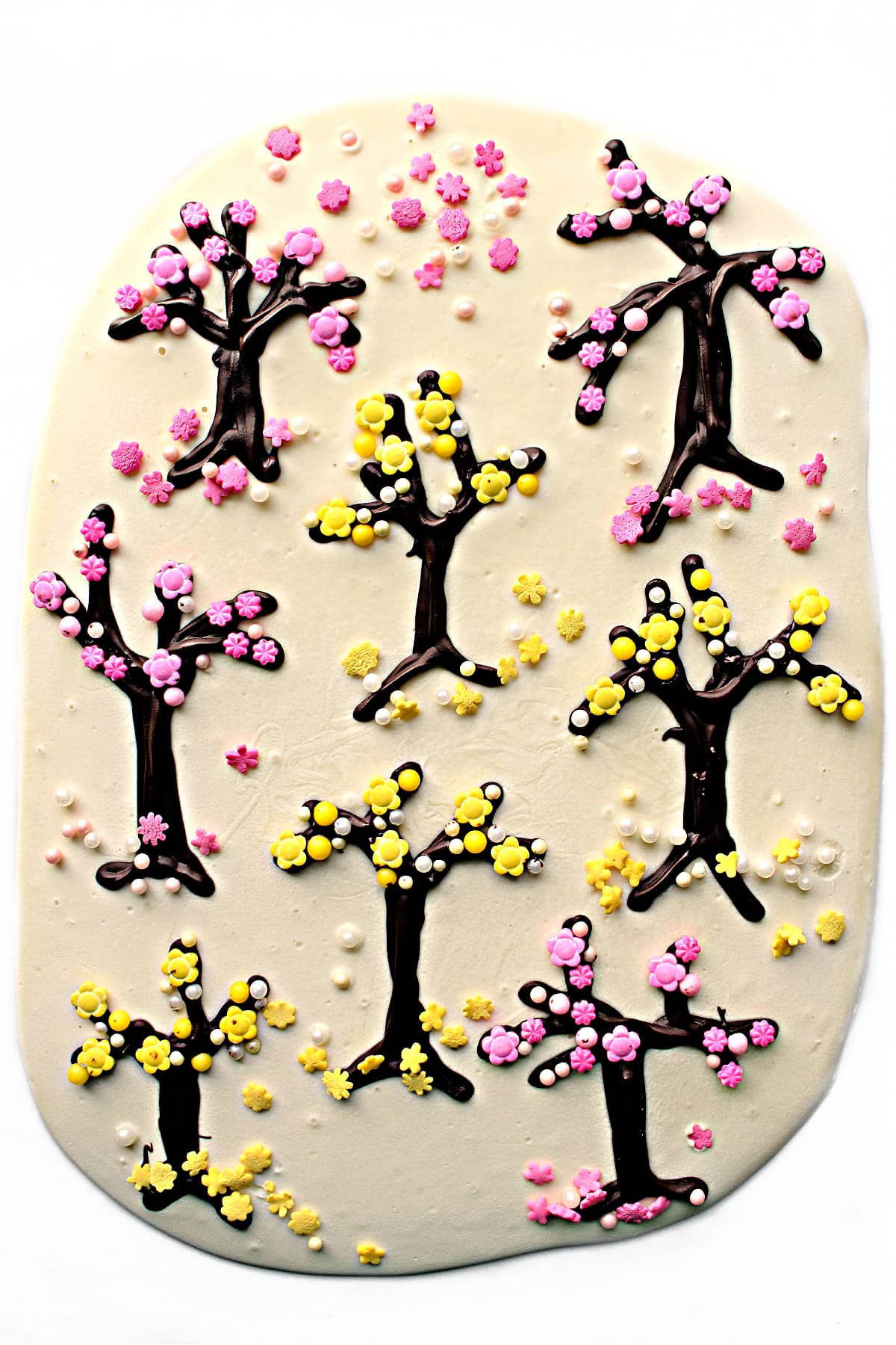 White Chocolate Bark  with white chocolate background, piped chocolate trees, and pink and yellow sprinkle blossoms. 
