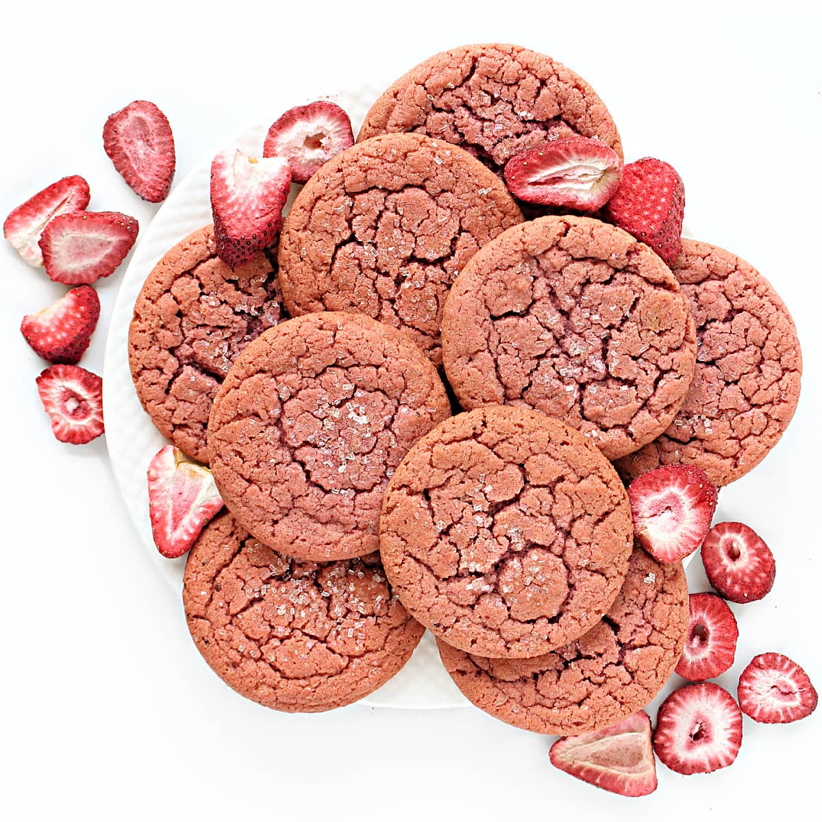 Plate of pink, strawberry cookies with cracked tops and decorating sugar with some freeze dried strawberries.