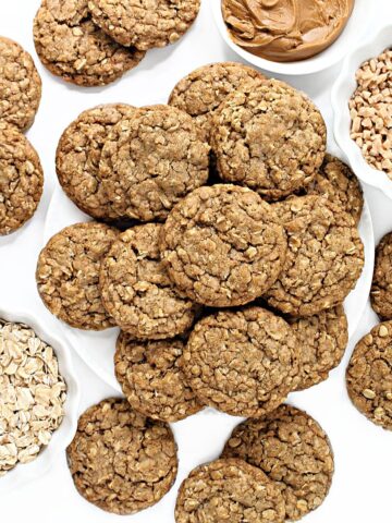 Round oat cookies with cracked tops with bowls of oats, toffee bits, and cookie butter.