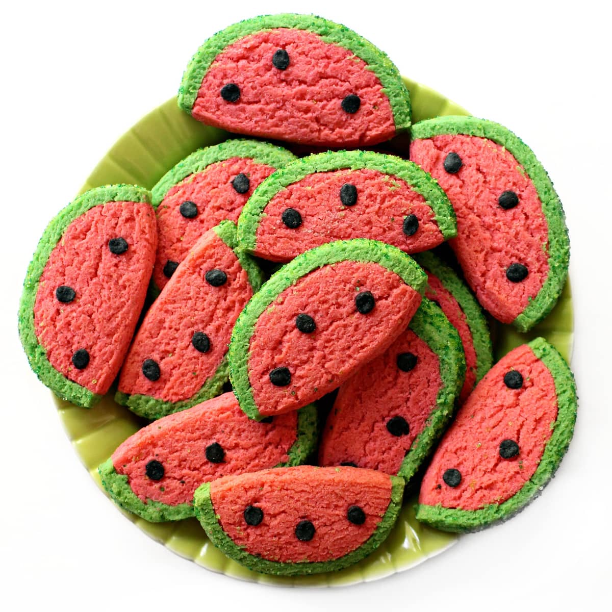 Platter of semi circle cookies with pink centers and green edges and black  dots for seeds.