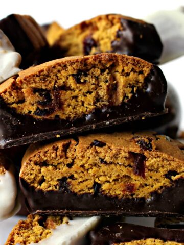 Closeup of 2 pumpkin biscotti with cranberries and bottoms dipped in chocolate.