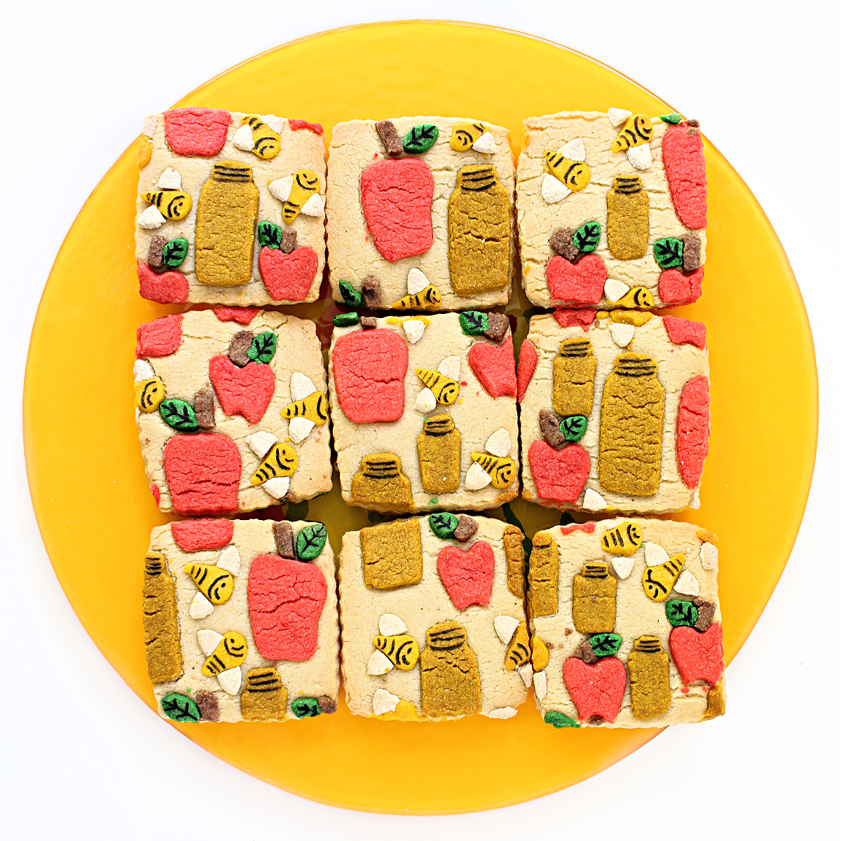 Square sugar cookies decorated with cutout bees, apples, and honey jars.