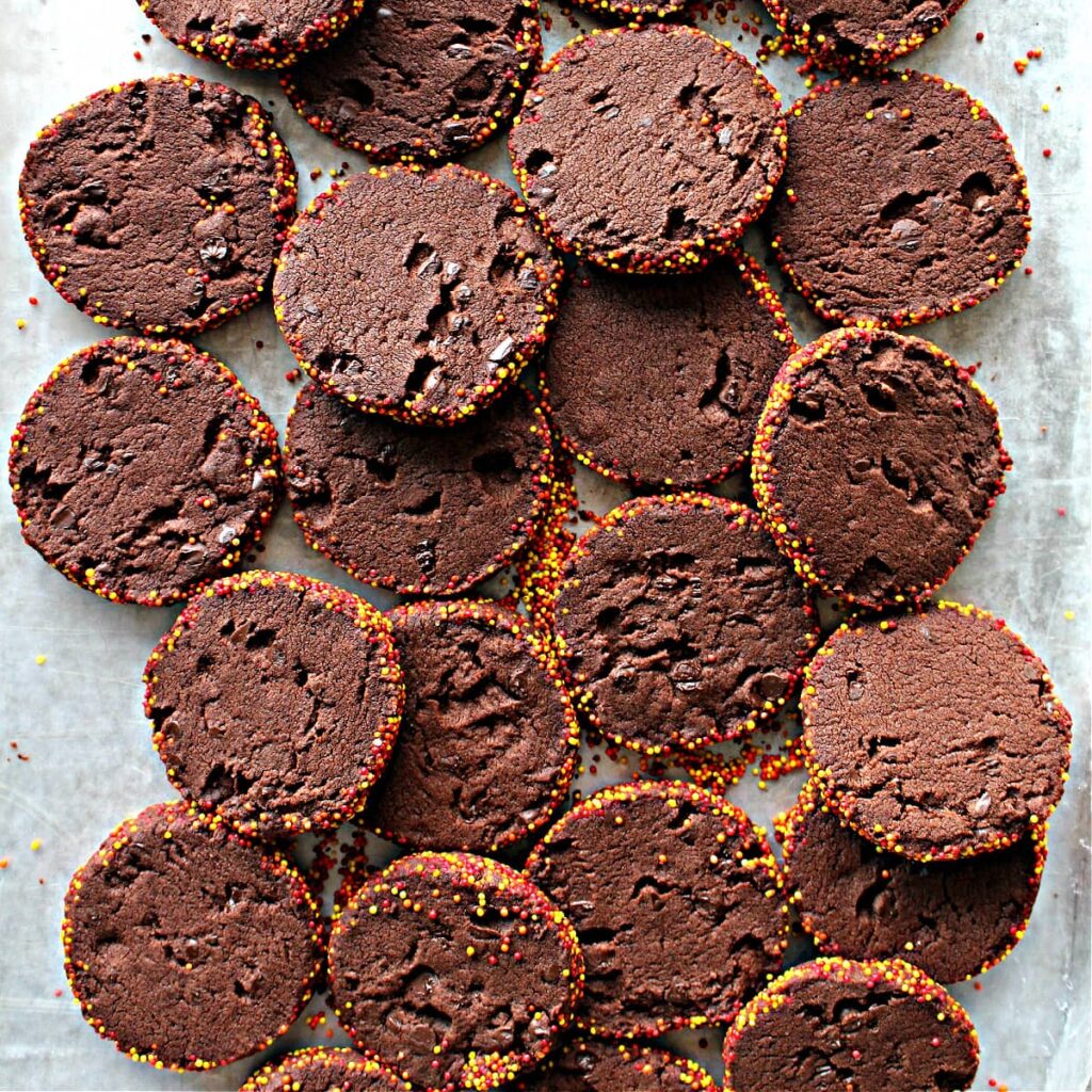 Sliced chocolate cookies with chocolate chips in the dough and sprinkles on the edges.