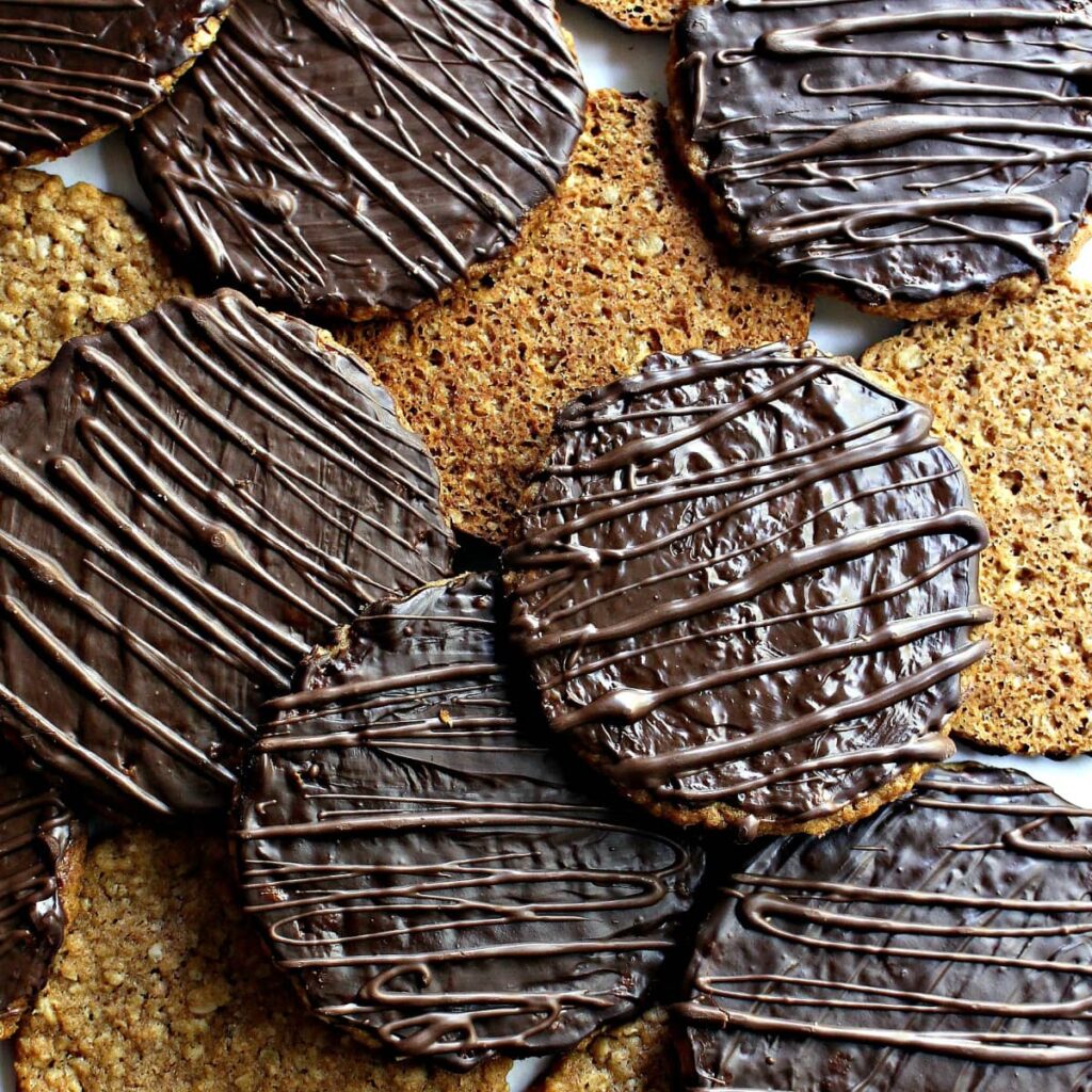 Flat, round oat cookies with bottoms coated in chocolate with a chocolate drizzle.