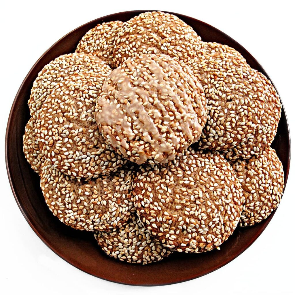 Sesame seed coated cookies with an icing drizzle on a serving plate.