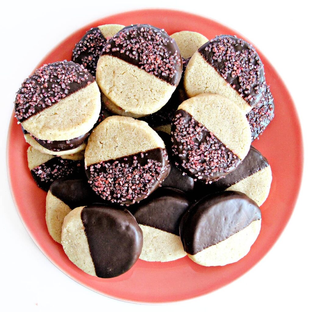 Round, sliced shortbread cookies half dipped in chocolate with large crystal sugar sprinkles.