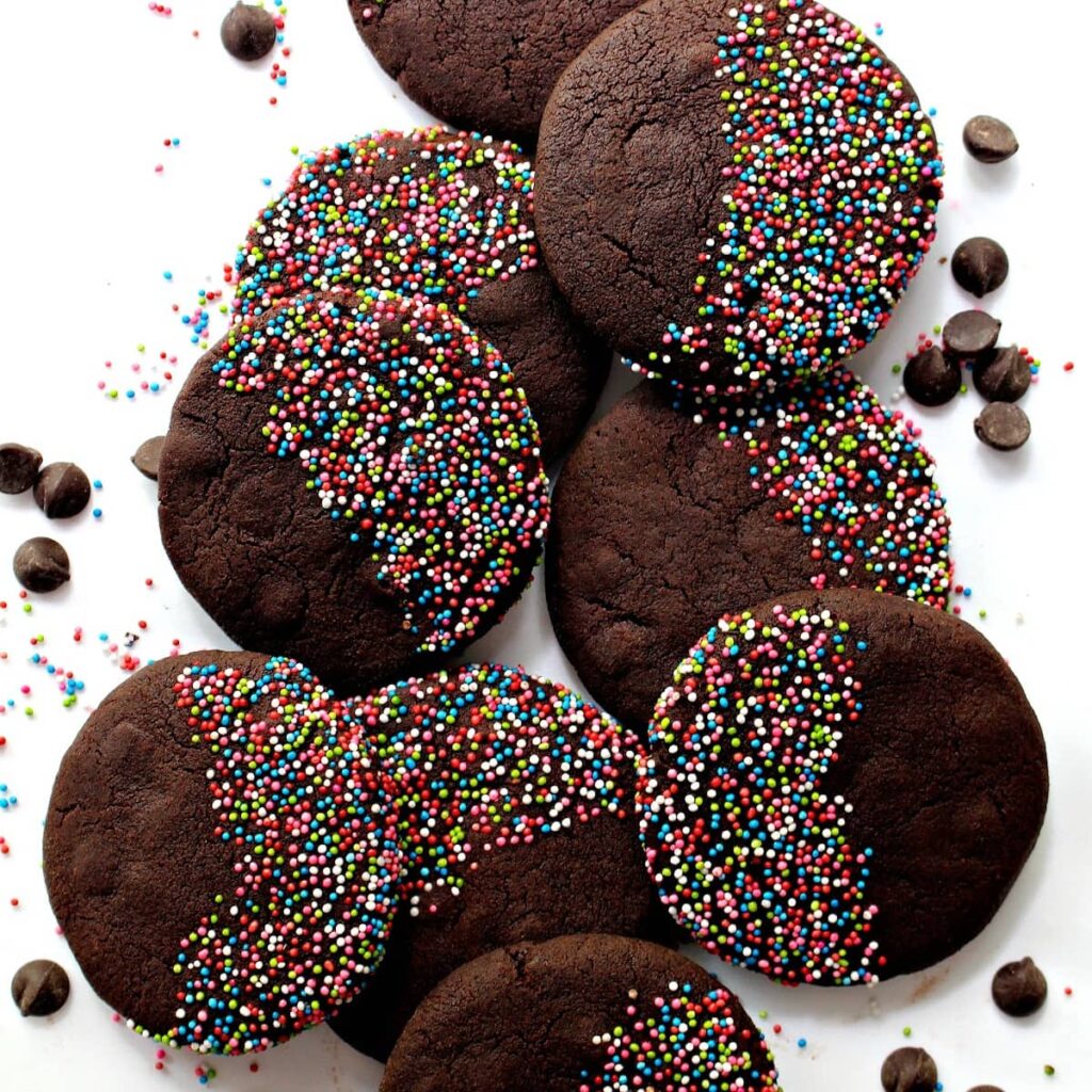 Flat, round chocolate cookies half covered with nonpareil sprinkles.