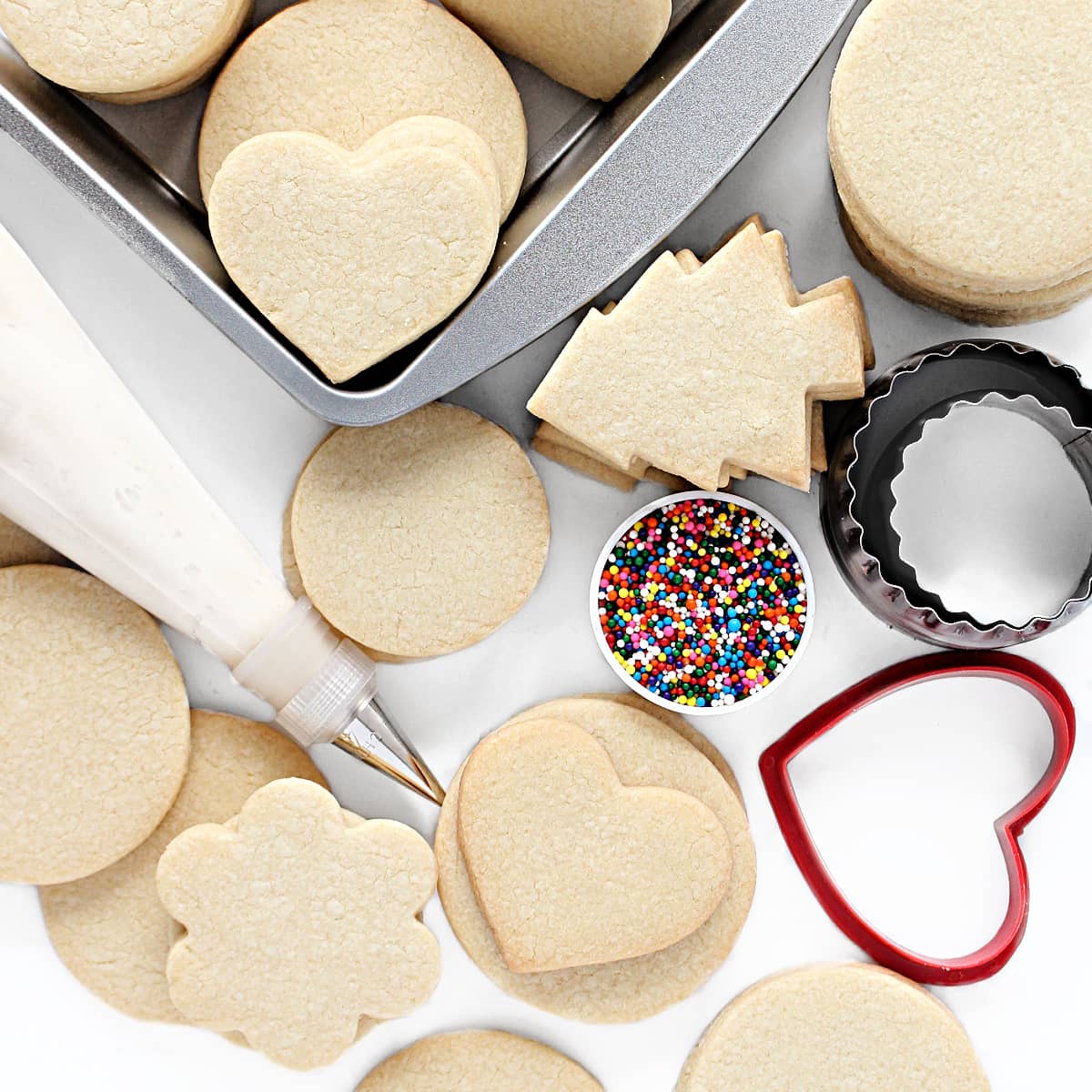 Stacks of  cut out vanilla sugar cookies with an icing bag and sprinkles for decorating.