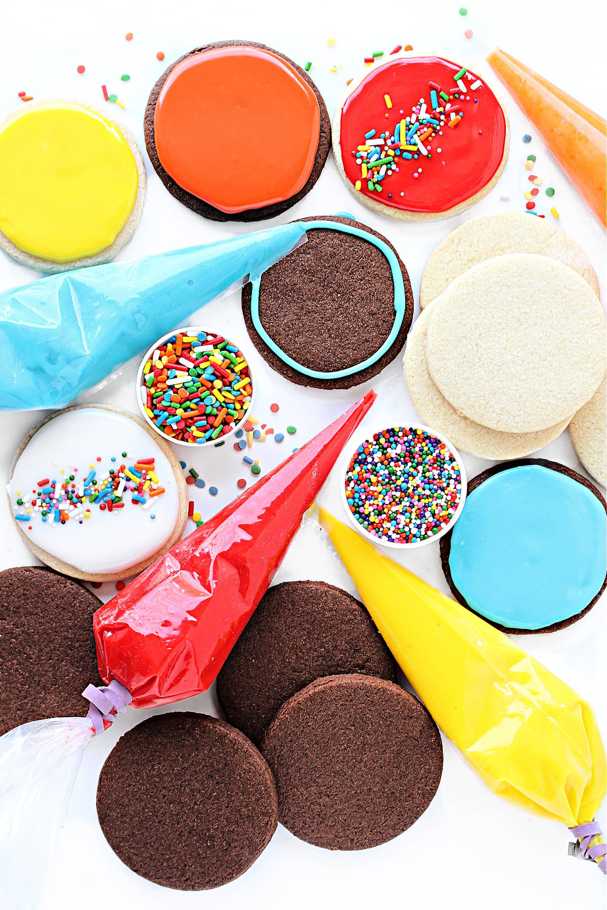 Colorful icing glaze in piping bags, chocolate and vanilla sugar cookie circles, and sprinkles.