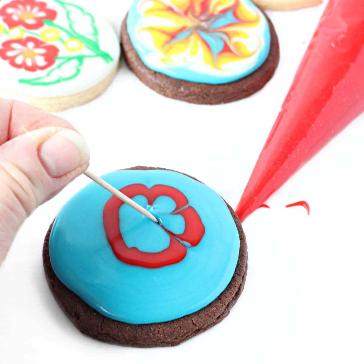 Dragging toothpick in glaze icing on  a chocolate sugar cookie to make a flower.