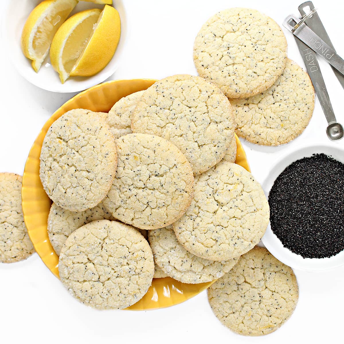 A serving plate piled with Lemon Poppy Seed Cookies with crackled tops, poppy seeds speckling the dough, and golden edges cookies.