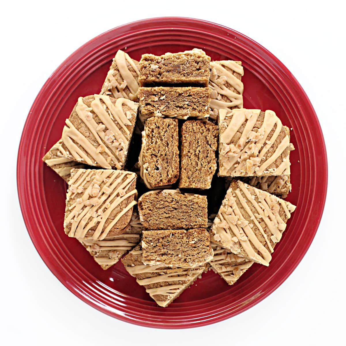 A serving plate filled with Biscoff Blondie bars topped with drizzled Biscoff icing and sprinkled with crunchy toffee bits.