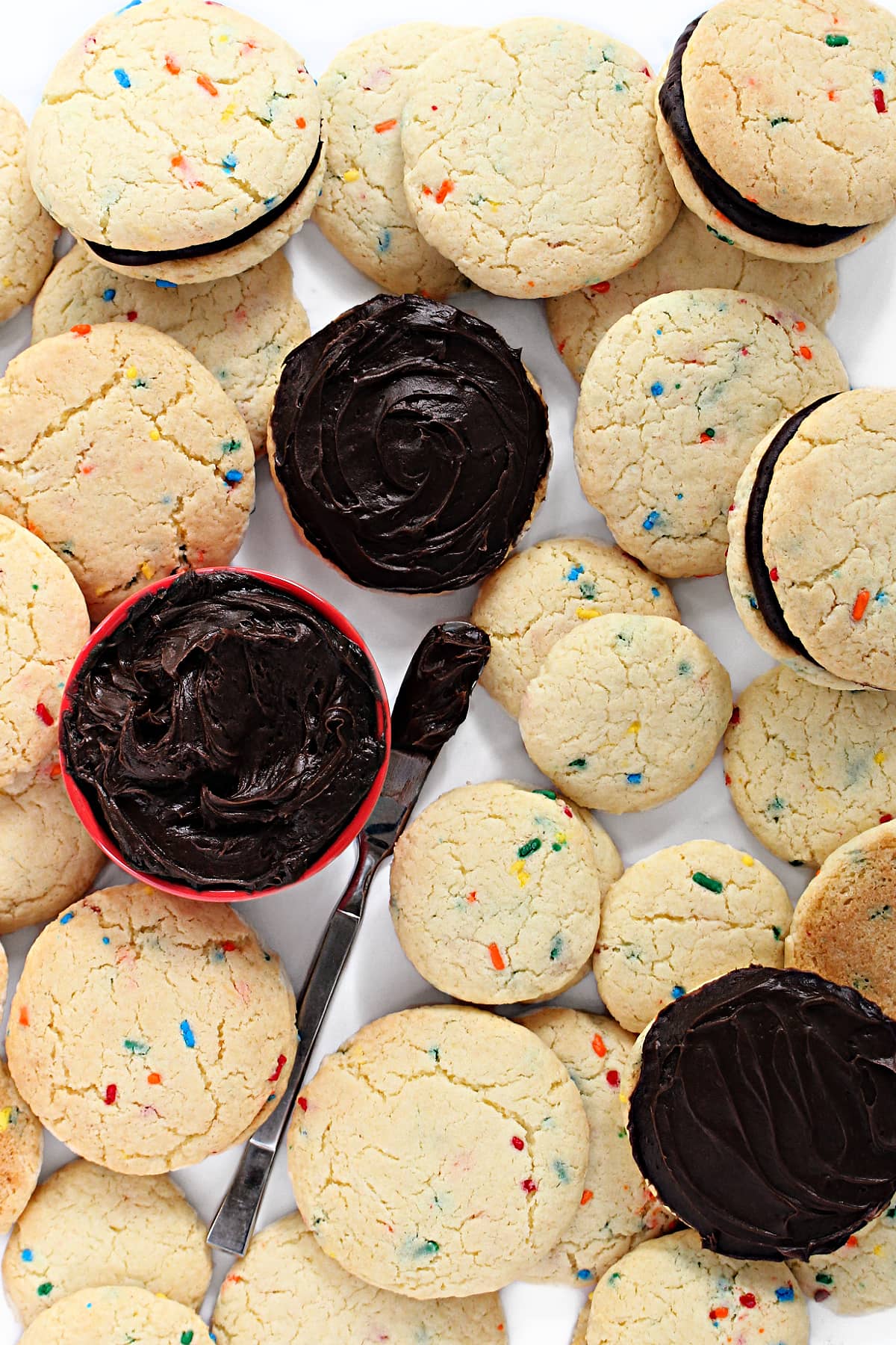 Fluffy Funfetti Cake Mix Cookies speckled with colorful jimmies sprinkles in the dough and chocolate frosting for making sandwich cookies.