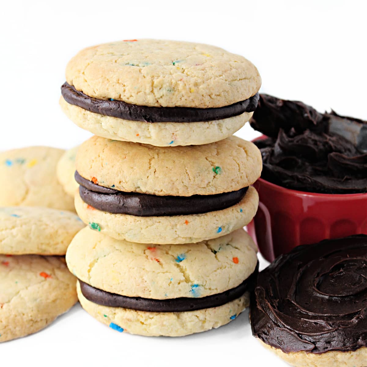 Stacked sandwich cookies made from Funfetti Cake Mix Cookies with chocolate frosting in the middle.